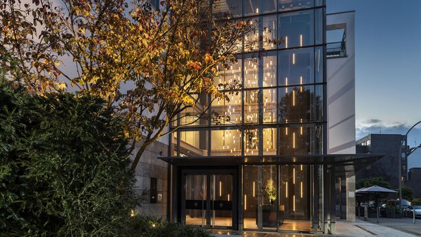 A modern building with a glass facade, a well-lit entrance, and a tree in the foreground.