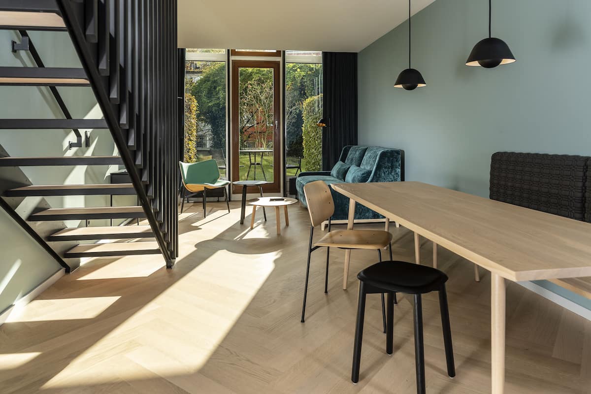 Un interior moderno con una mesa de comedor de madera, sillas negras, un sofá azul y una escalera con barandillas negras.