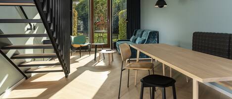 A modern interior with a wooden dining table, black chairs, a blue sofa, and a staircase with black railings.