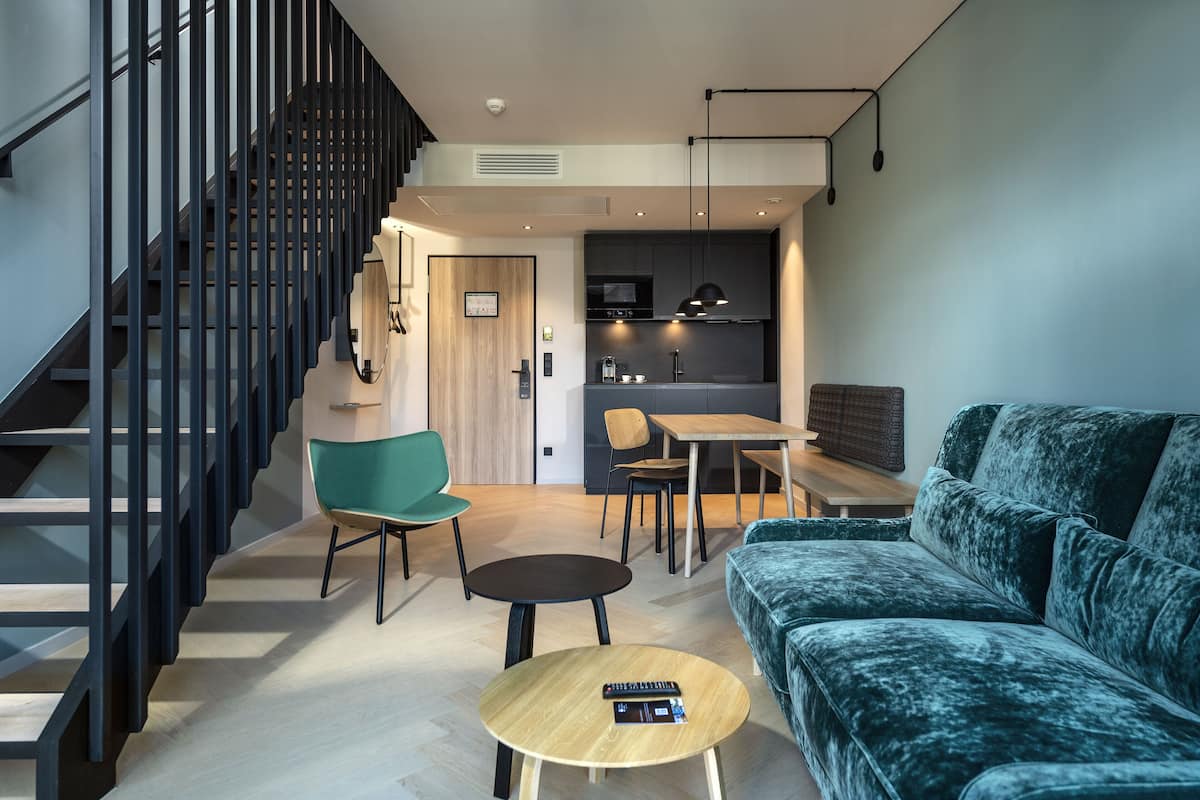 Una sala de estar moderna con una escalera, un sofá, una mesa de comedor y una zona de cocina.