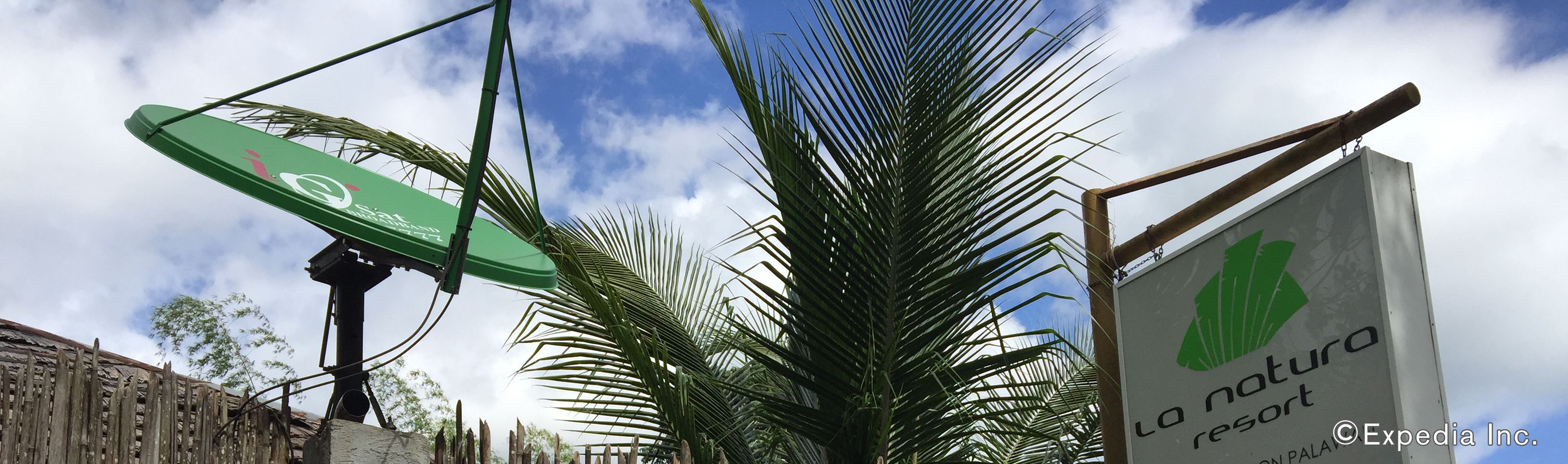 A sign for La Naturaleza Resort with a palm tree in the foreground.