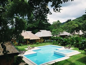 A pool area with lounge chairs, a thatched-roof building, and lush greenery. - La Natura Resort (Coron)