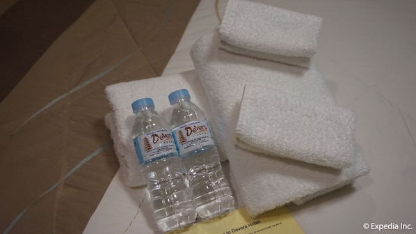 A Devera Hotel room with two Devera water bottles, a white towel, and a yellow note on the bed. - Devera Hotel (Angeles City)