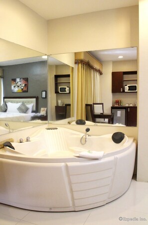 A modern bathroom with a large freestanding bathtub, a mirror, a microwave, and a small refrigerator. - Devera Hotel (Angeles City)