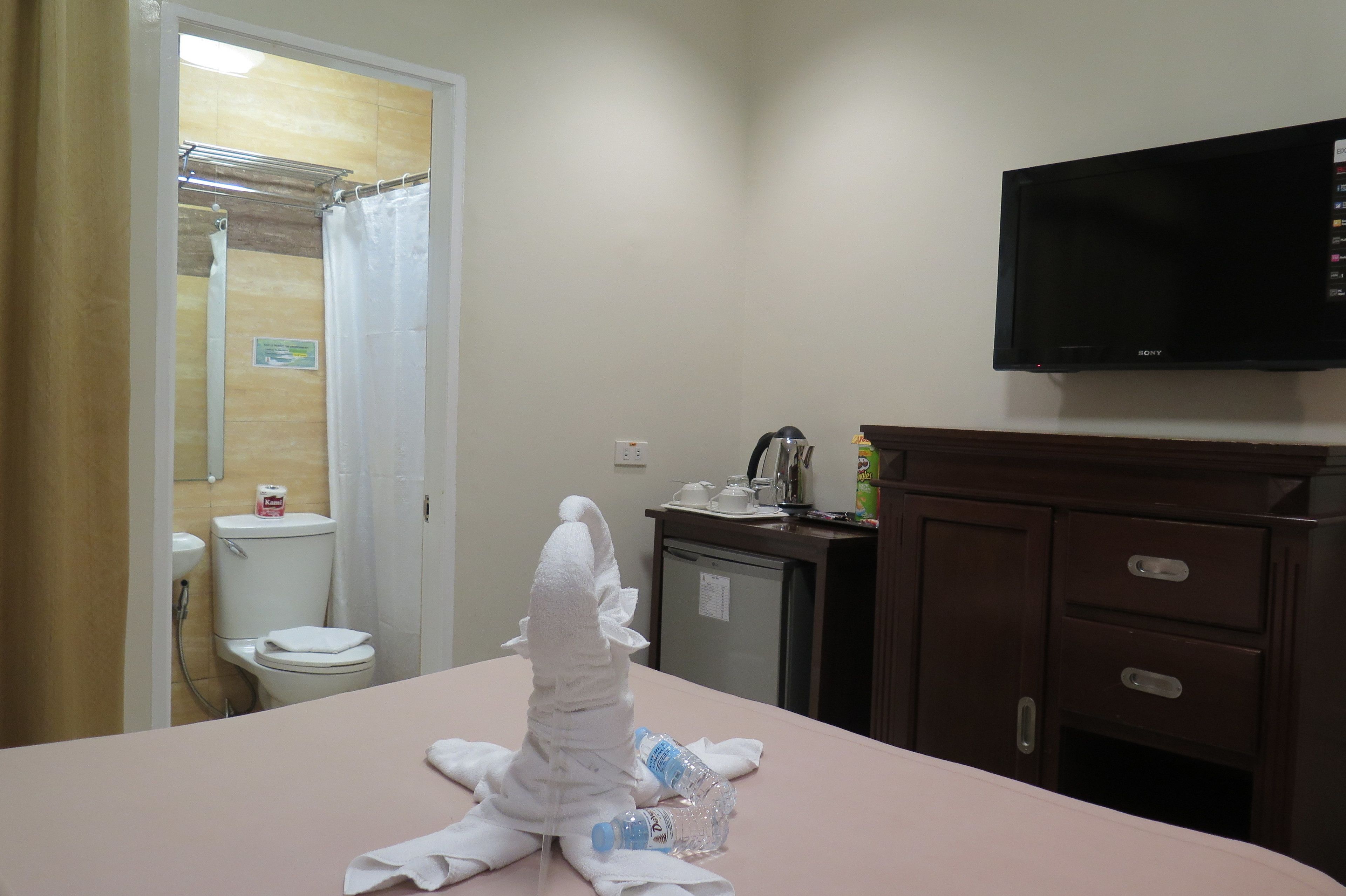 A hotel room with a bed, a television mounted on the wall, a small cabinet, and a bathroom visible through an open door.