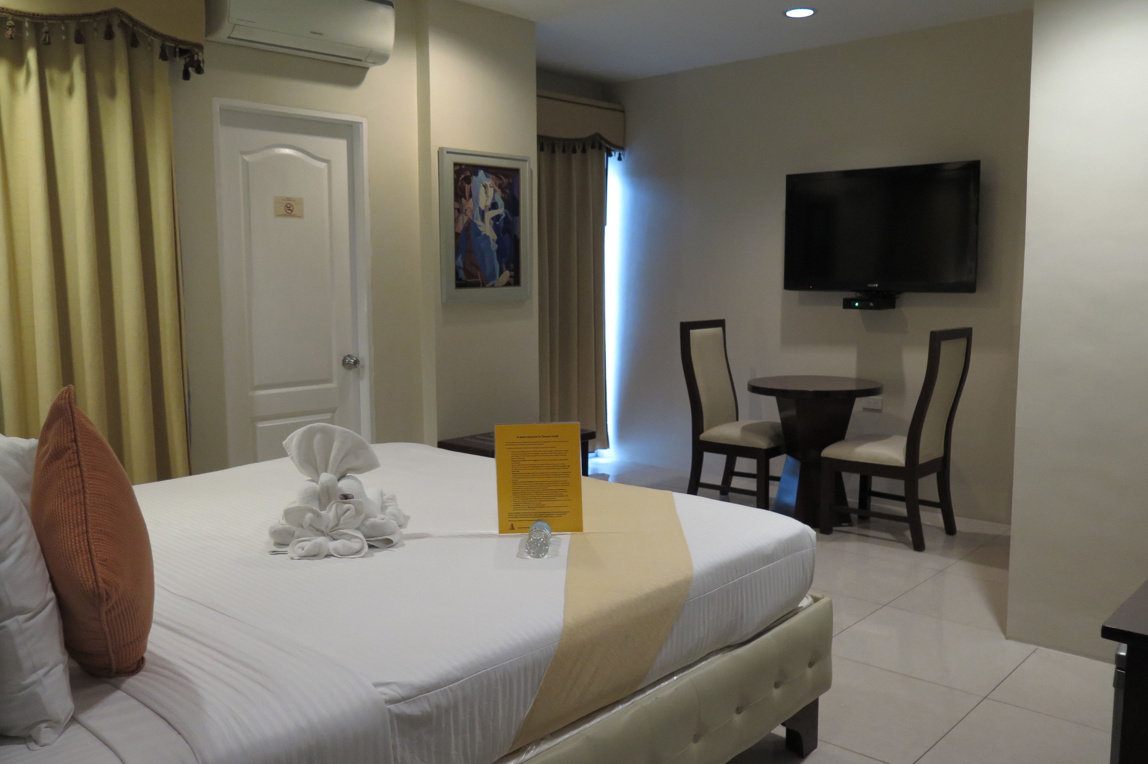 A hotel room with a bed, a desk, a chair, a television, and a painting on the wall.