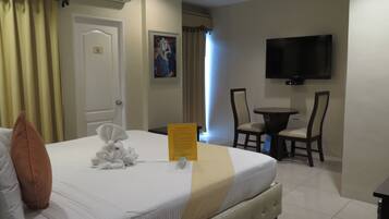 A hotel room with a bed, a desk, a chair, a television, and a painting on the wall.