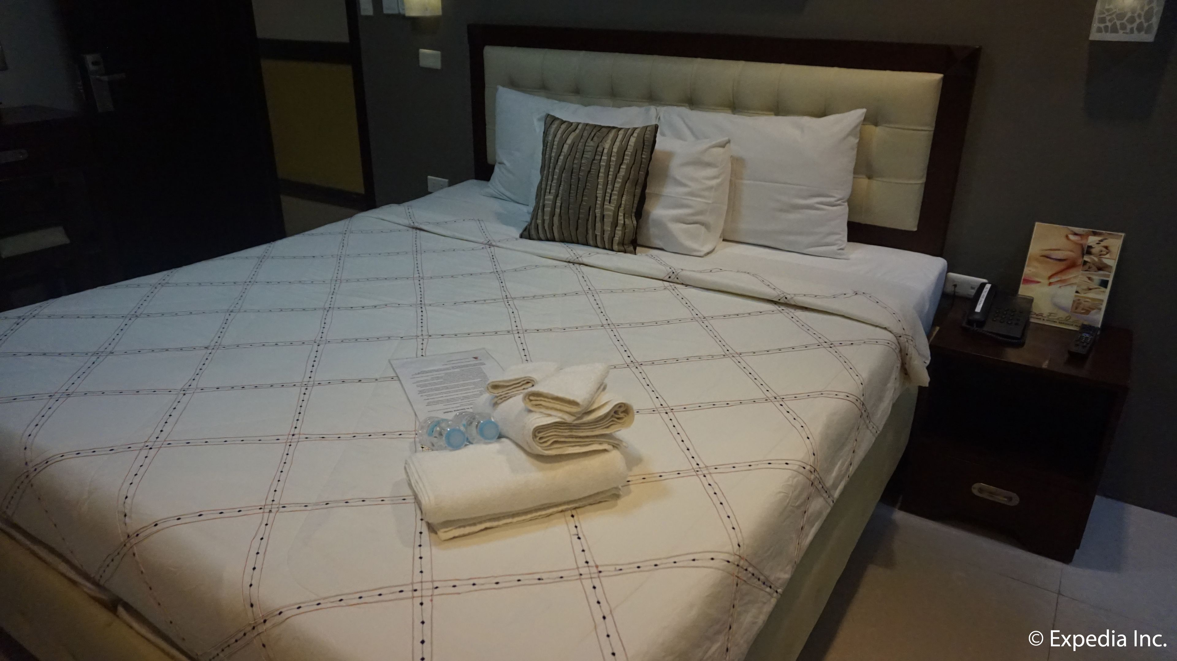 A neatly made bed with a checkered bedspread, a folded towel, and a water bottle on the bed.