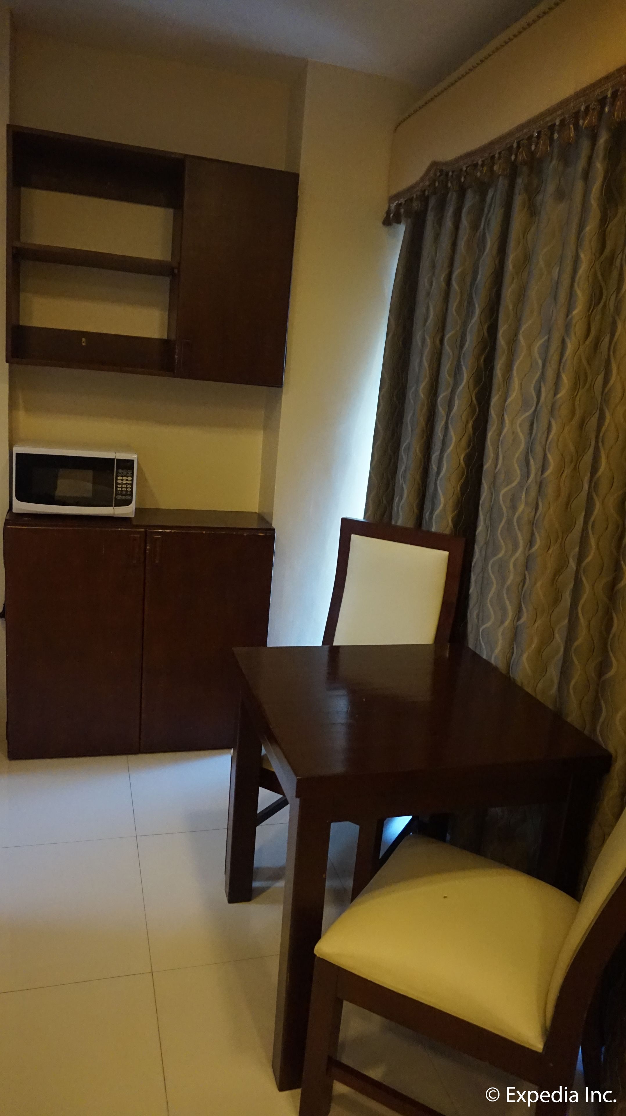 A compact kitchen with a microwave, a wooden cabinet, and a dining table with a chair.