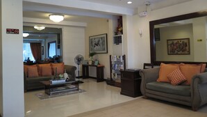 A living room with a sofa, a coffee table, and a fan. There is a sign on the wall and a framed picture above the sofa. - Devera Hotel (Angeles City)
