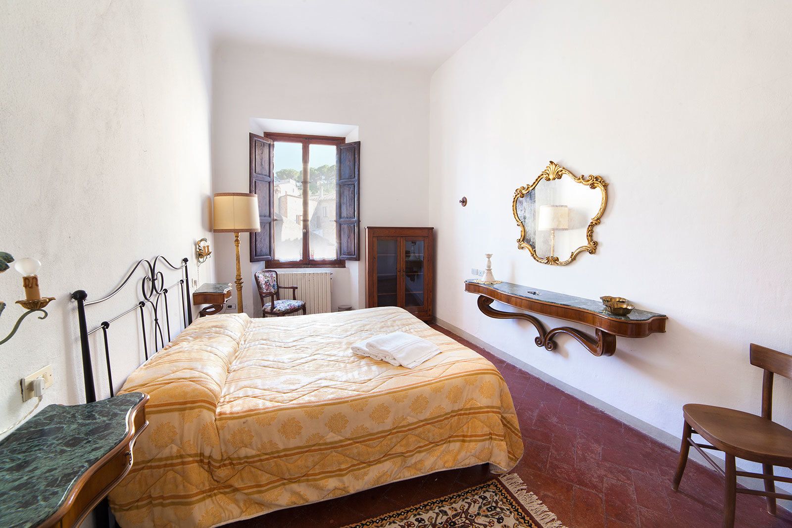 A bedroom with a bed, a chair, a dresser, a mirror, and a window.