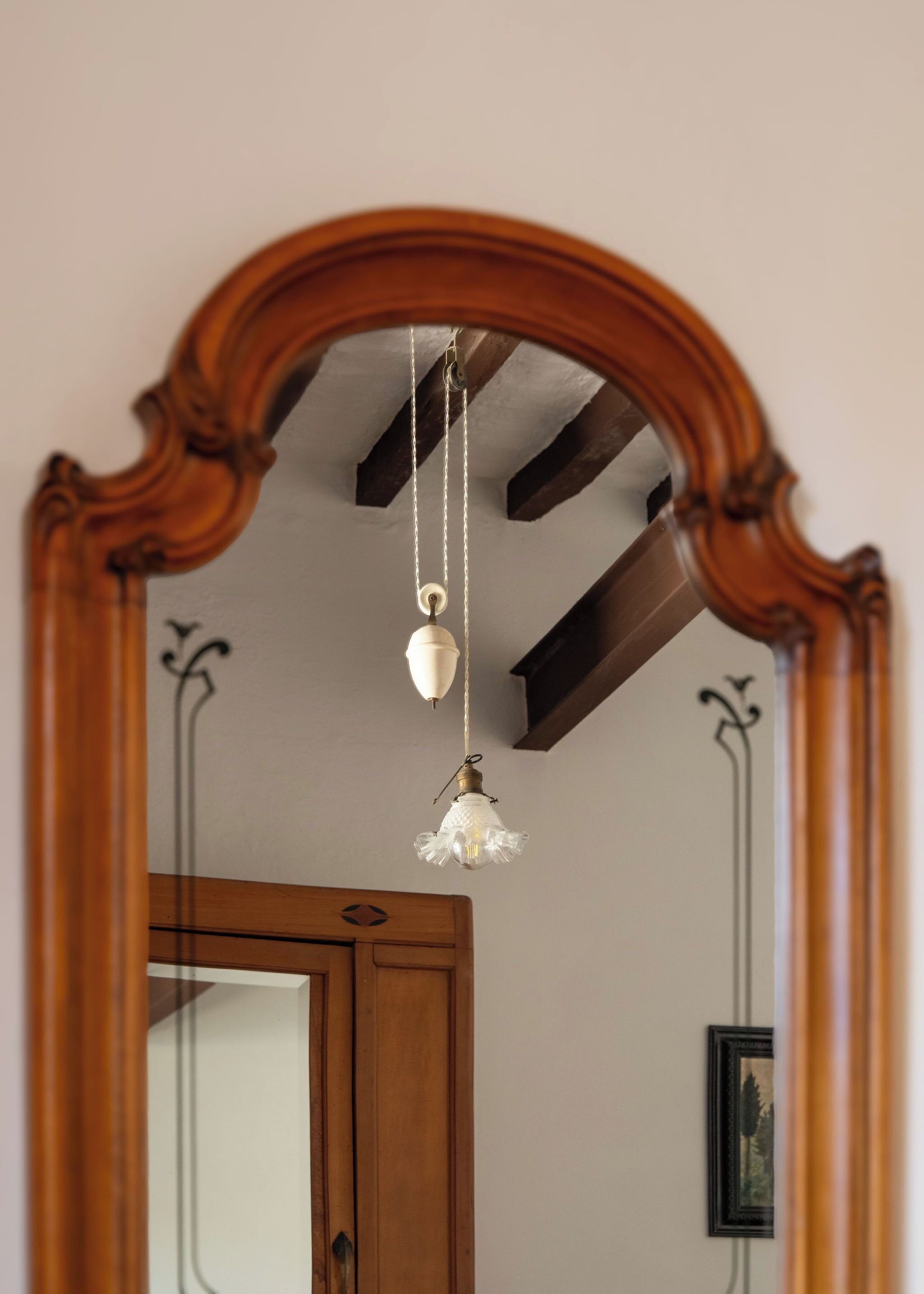 A mirror with an ornate wooden frame, a ceiling fan, and a hanging light fixture.