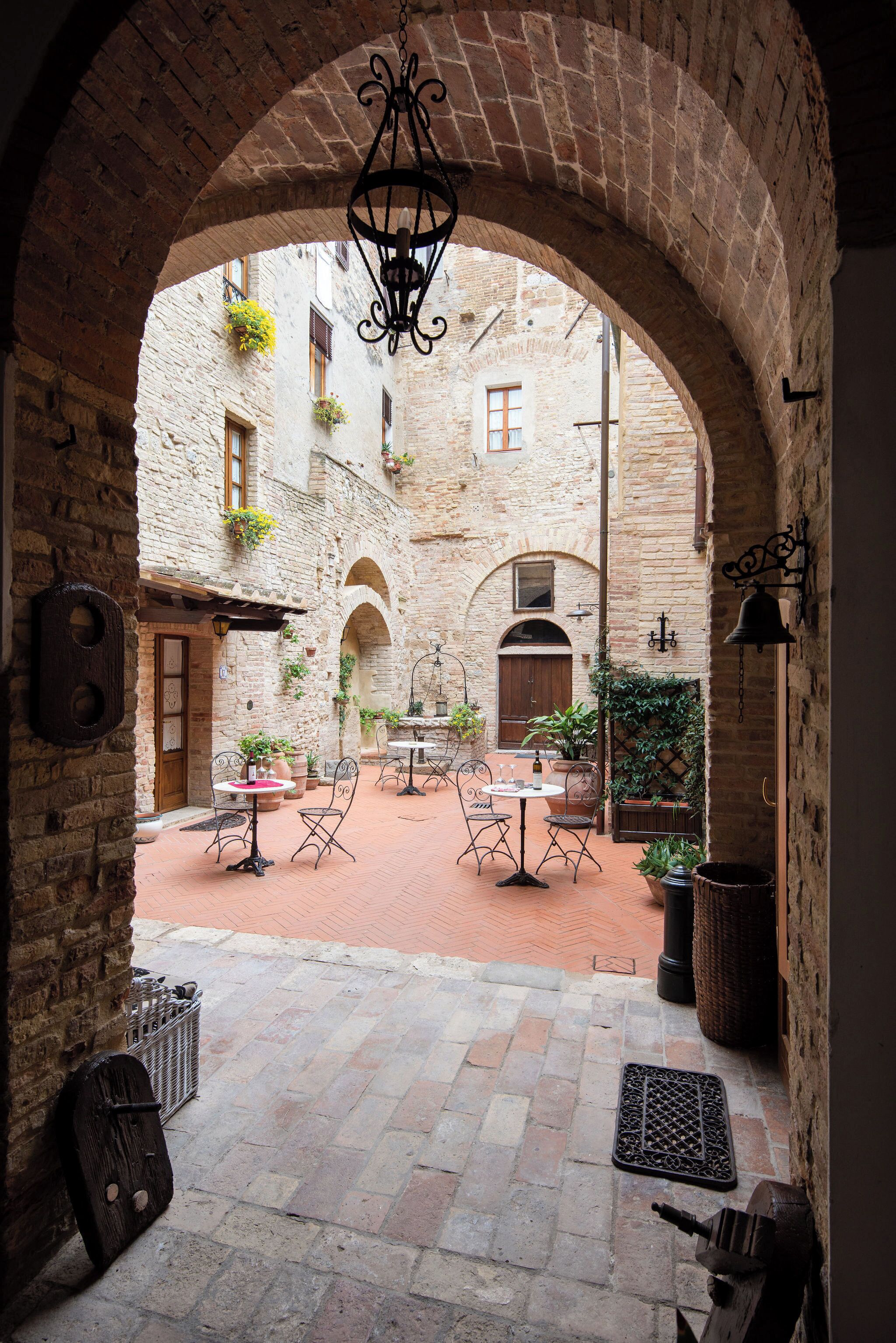 Un patio arqueado con muros de ladrillo, un farol colgante y asientos al aire libre.