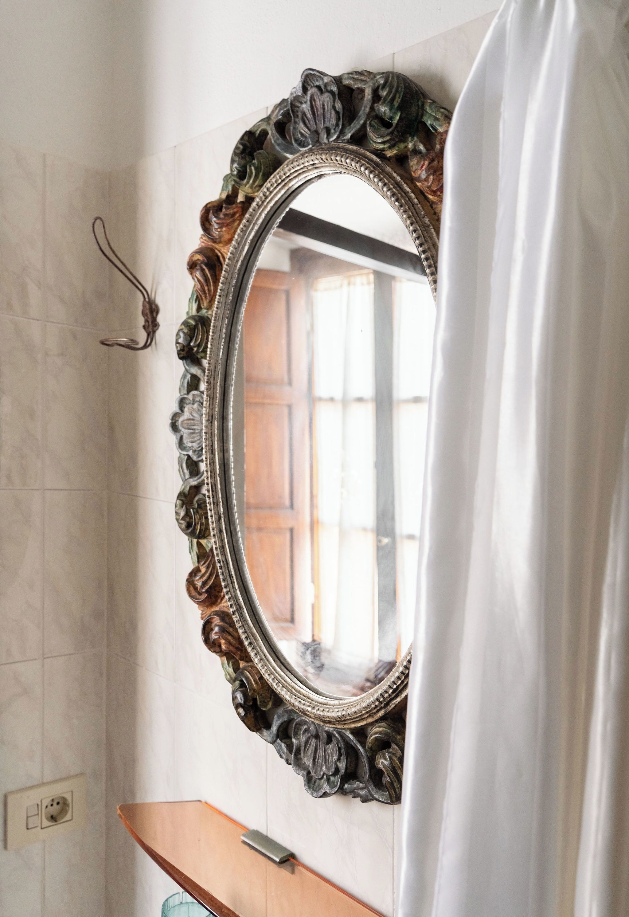 A bathroom with a large ornate mirror, a wooden vanity, and a towel hanging on the right.