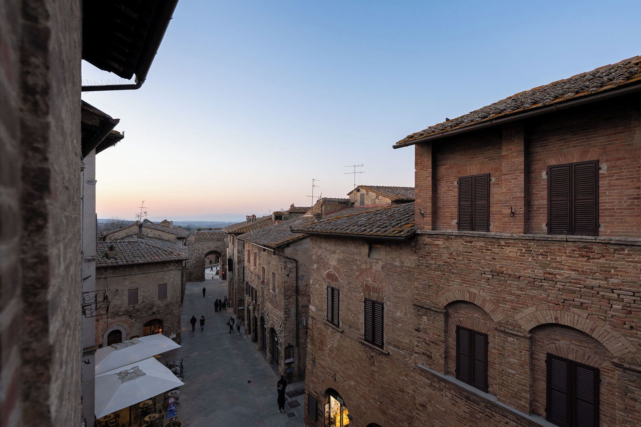 A narrow street with traditional brick buildings, arched doorways, and a clear sky.