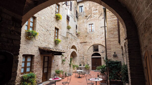 An outdoor courtyard with stone walls, arched doorways, and potted plants. - Residenza d'Epoca Palazzo Buonaccorsi (San Gimignano)