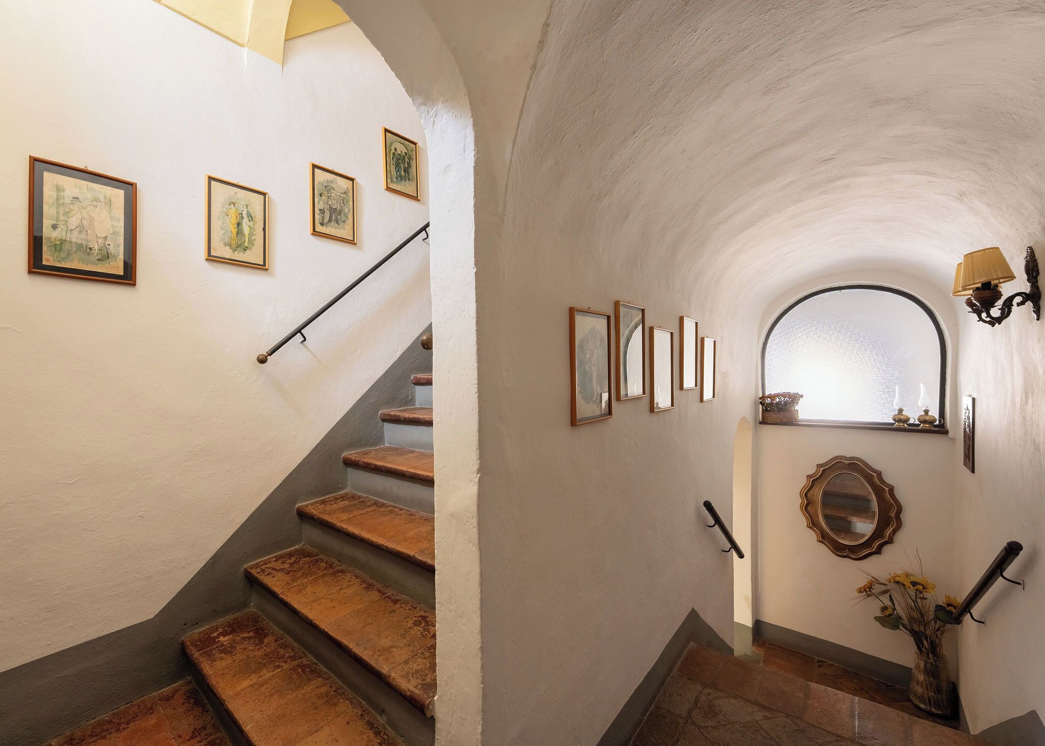 Un escalier avec des marches en bois et une rampe, bordé de murs ornés d’œuvres d’art encadrées et d’un miroir.