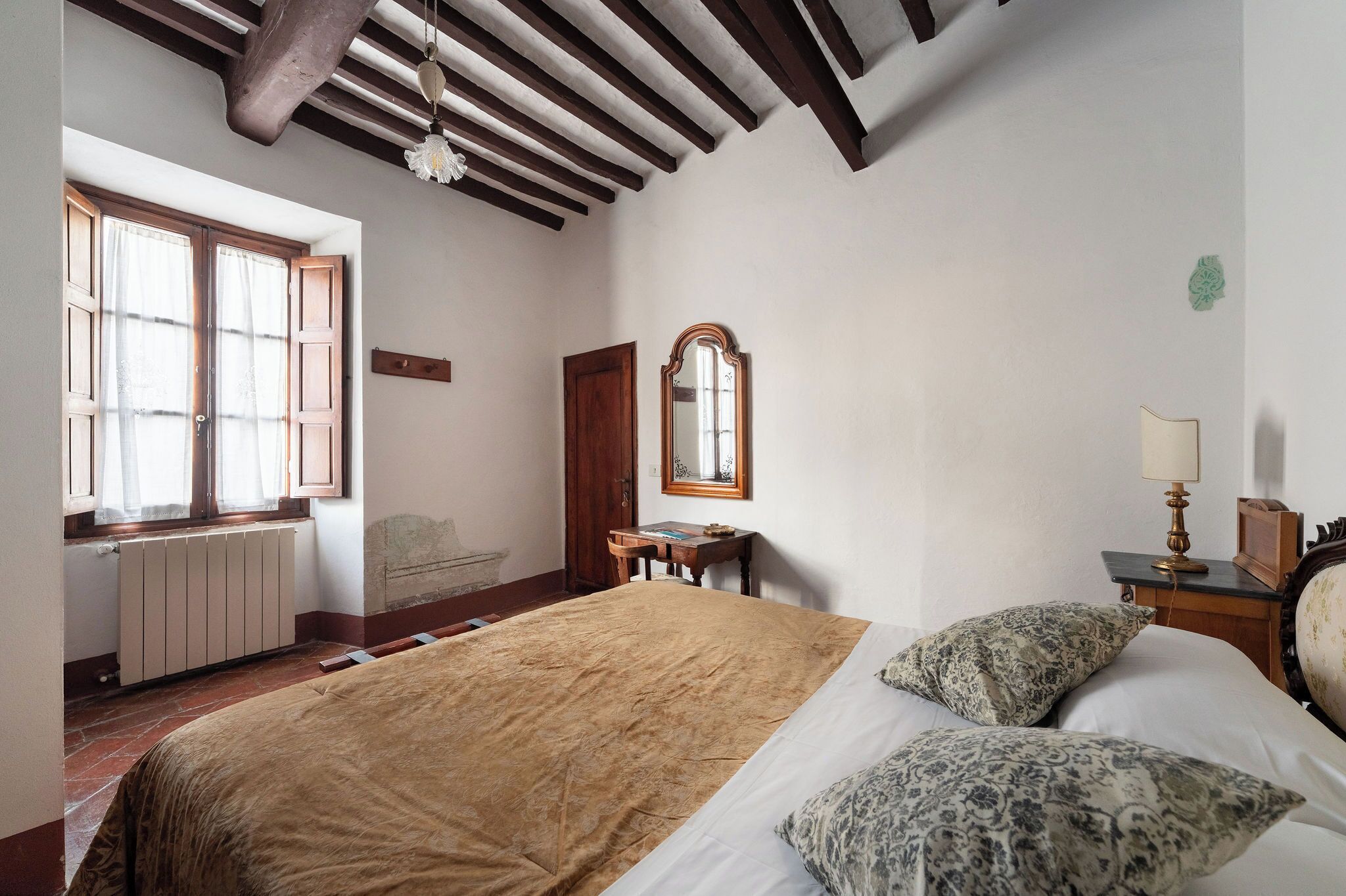 Un dormitorio con una cama grande, un escritorio de madera, un espejo y un radiador.