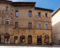 Un edificio storico con diverse finestre e porte ad arco, una facciata in mattoni e un tetto piano.