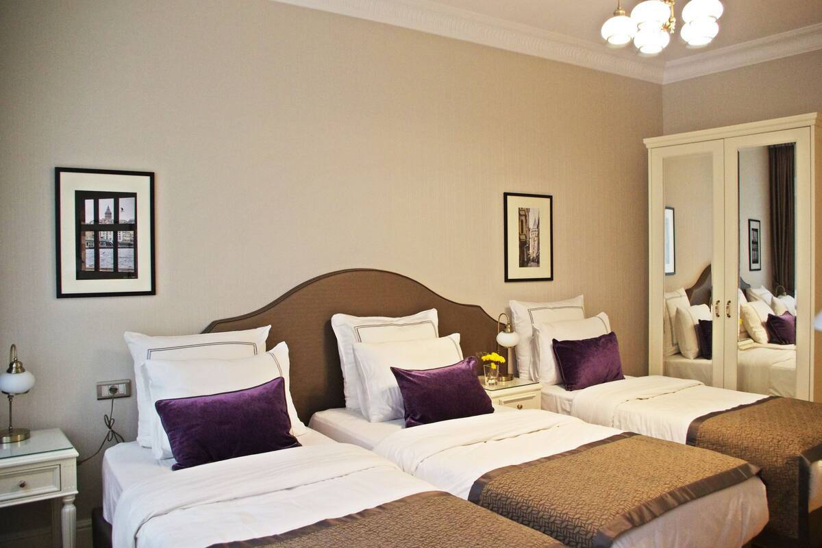 A hotel room with two single beds, a nightstand with a lamp, and a large mirror on the wall.