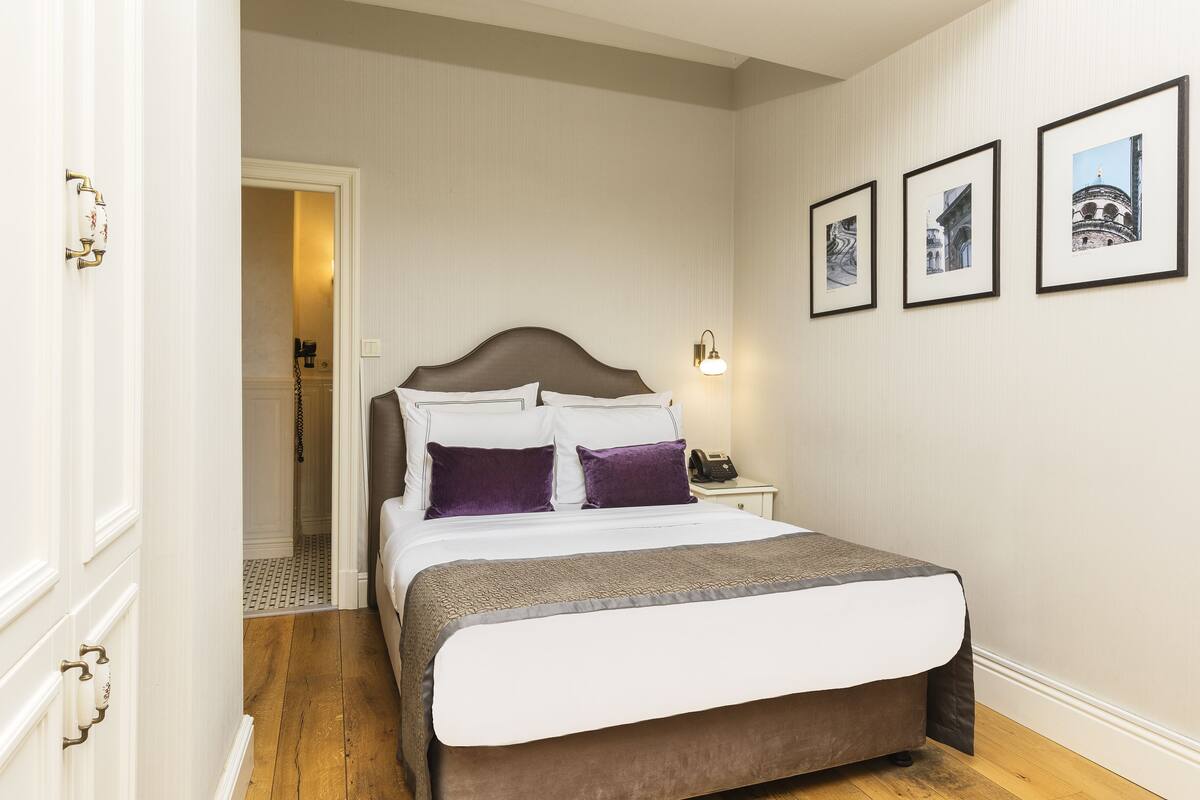 A neatly made bed with a headboard, a bedside table with a lamp, and three framed pictures on the wall.