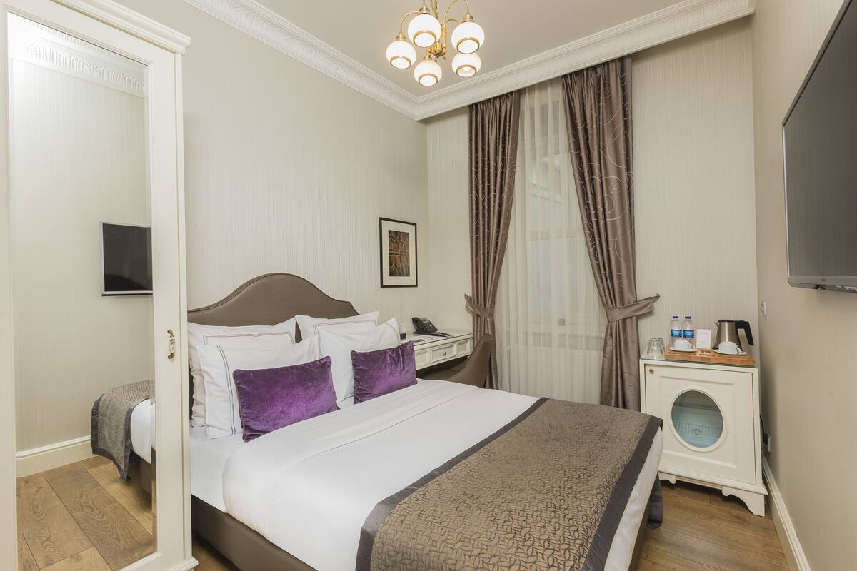 A neatly arranged hotel room with a large bed, a bedside table with a coffee maker, and a TV mounted on the wall.