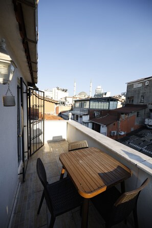 A balcony with a wooden table and chairs, a metal gate, and a view of buildings and a mosque in the distance. - Lemon Residence (Istanbul)