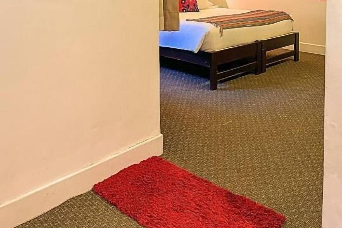 A hotel room with a bed, a red rug, a mirror, and a TV mounted on the wall.