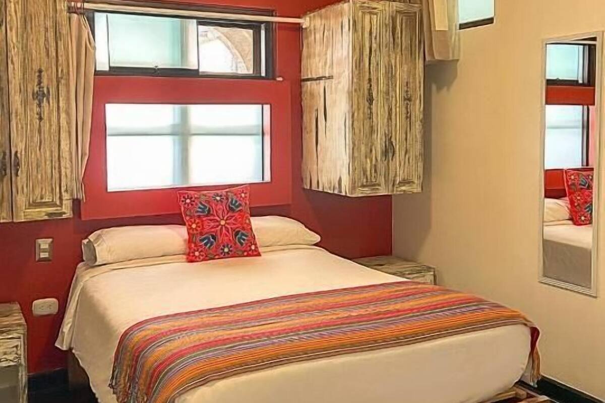 A room with a bed, a window with curtains, a mirror, and a light fixture.