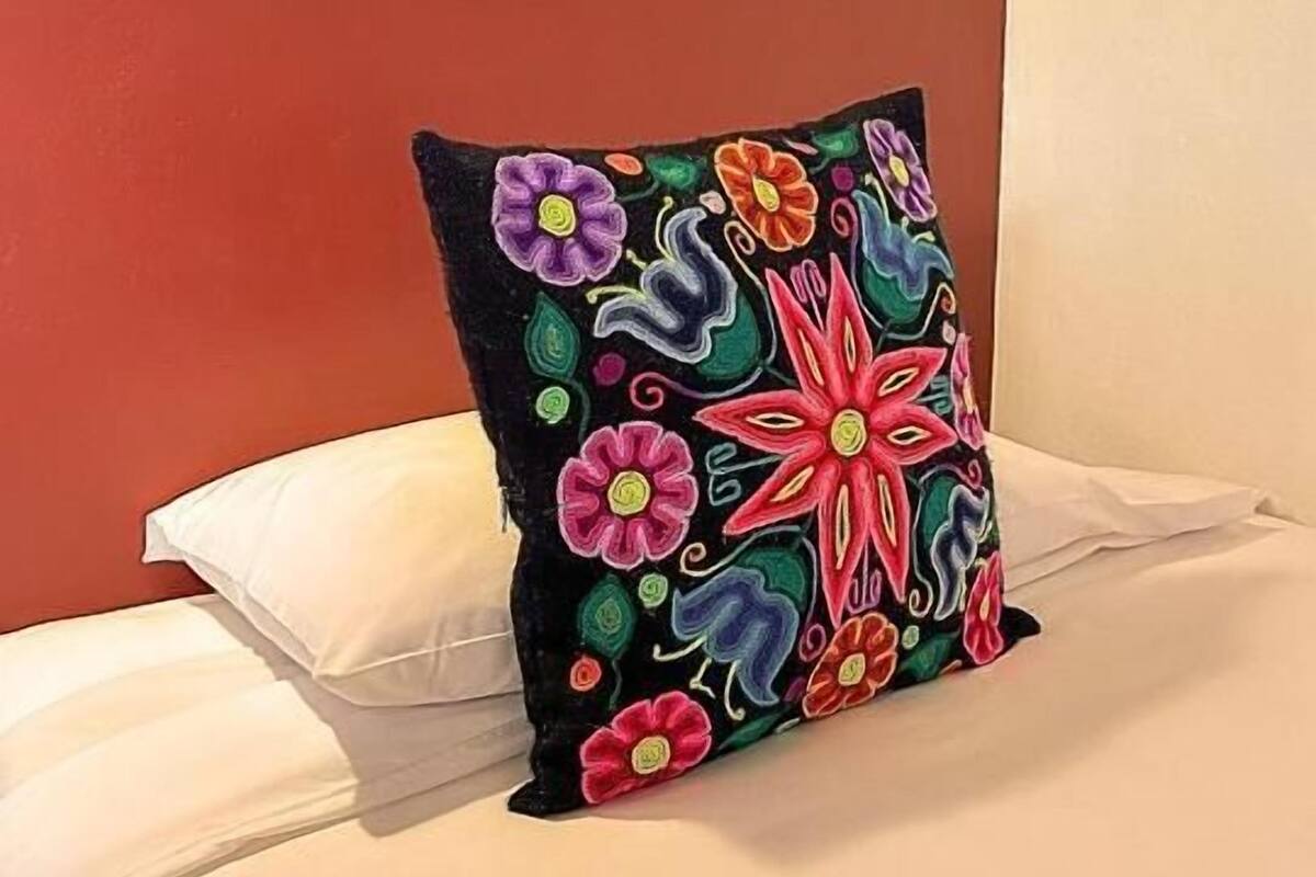A bed with a single white pillow and a colorful embroidered pillow.