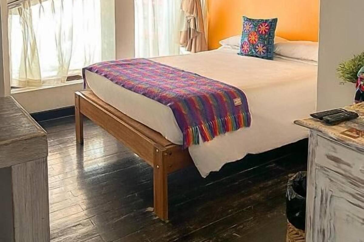 A bedroom with a wooden bed, a window with curtains, and a white wall.
