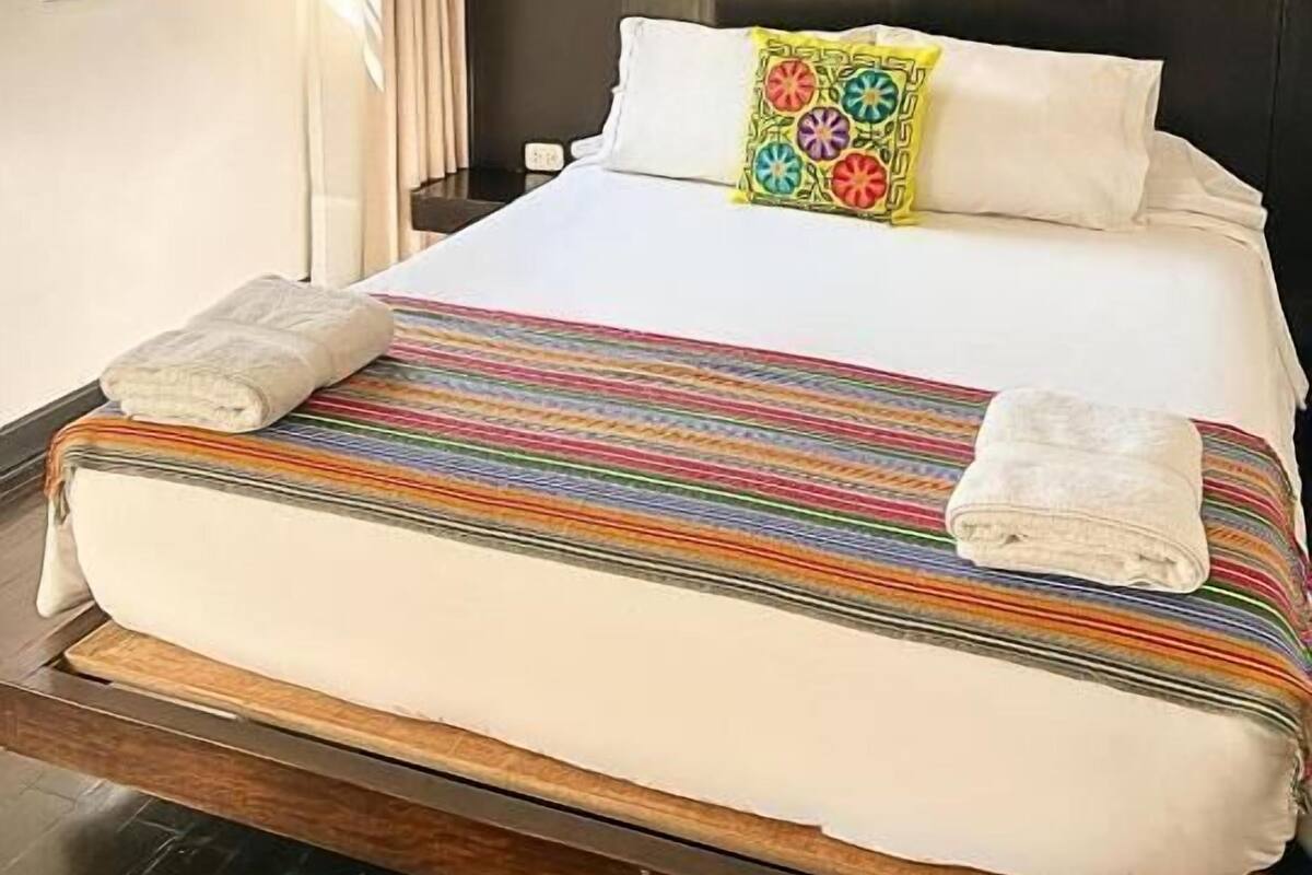 A hotel room with a bed, a window with curtains, and a teal accent wall.