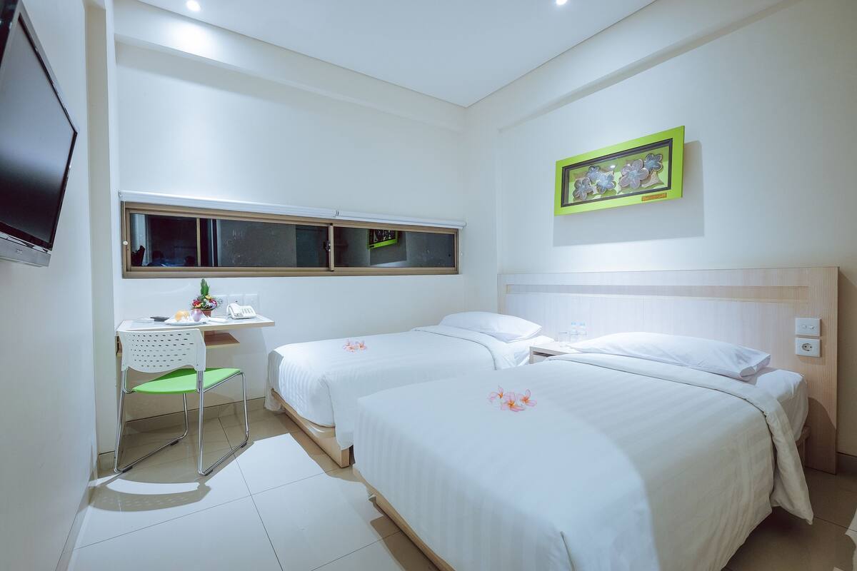 Une chambre d’hôtel avec deux lits, un bureau avec une chaise, une télévision et une fenêtre.