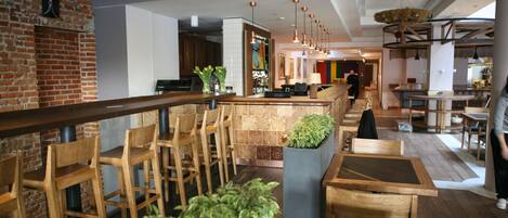 A modern restaurant interior with wooden furniture, a brick wall, and hanging pendant lights.