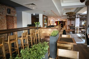 Un intérieur de restaurant moderne, avec des meubles en bois, un mur en briques et des luminaires suspendus.