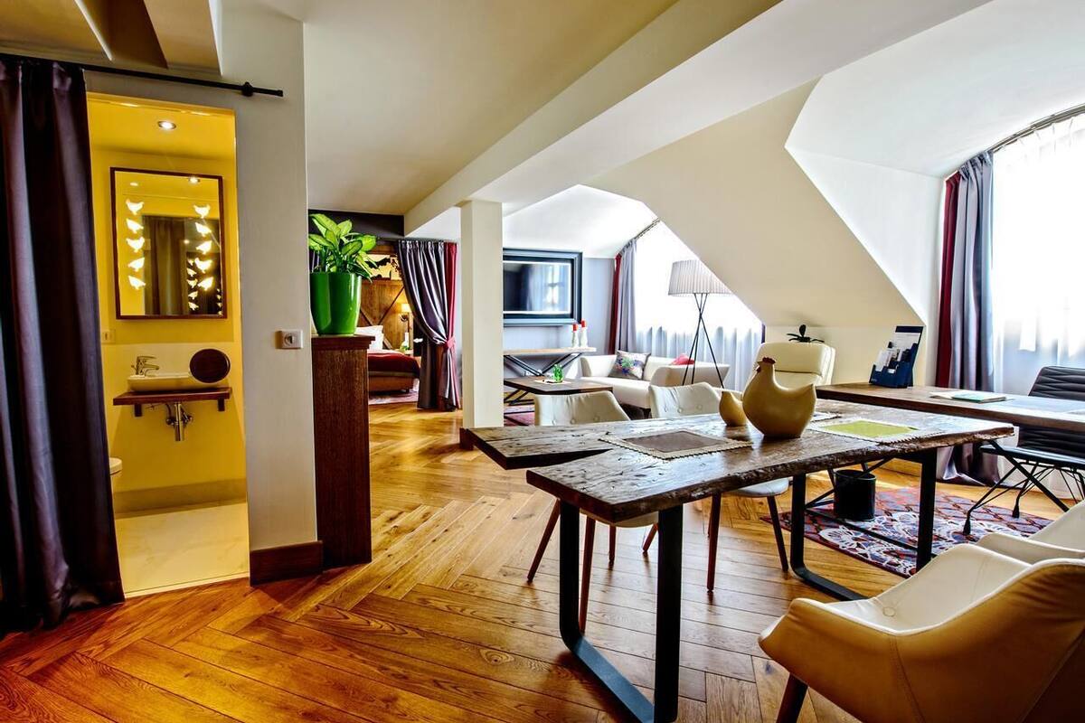 A spacious loft-style room with a wooden floor, a dining table, a sofa, and a TV.