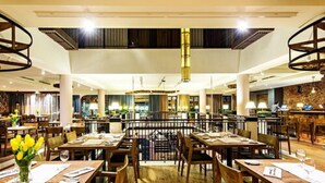 Um restaurante amplo com diversas áreas de refeição, mesas e cadeiras de madeira.