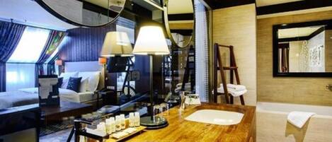 Habitación de hotel moderna con tocador de madera, dos lavamanos, un espejo grande y una cama con vista a la ciudad.