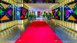 Um hall de hotel com carpete vermelho, paredes de vidro e padrões geométricos coloridos.