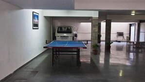 Un amplio espacio interior con mesa de ping pong, una furgoneta blanca y plantas en macetas.