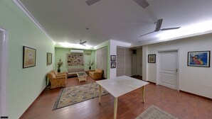 Una sala de estar con sofá, sillones, una mesa de centro y una mesa de comedor. Hay un ventilador de techo, una puerta y una ventana.