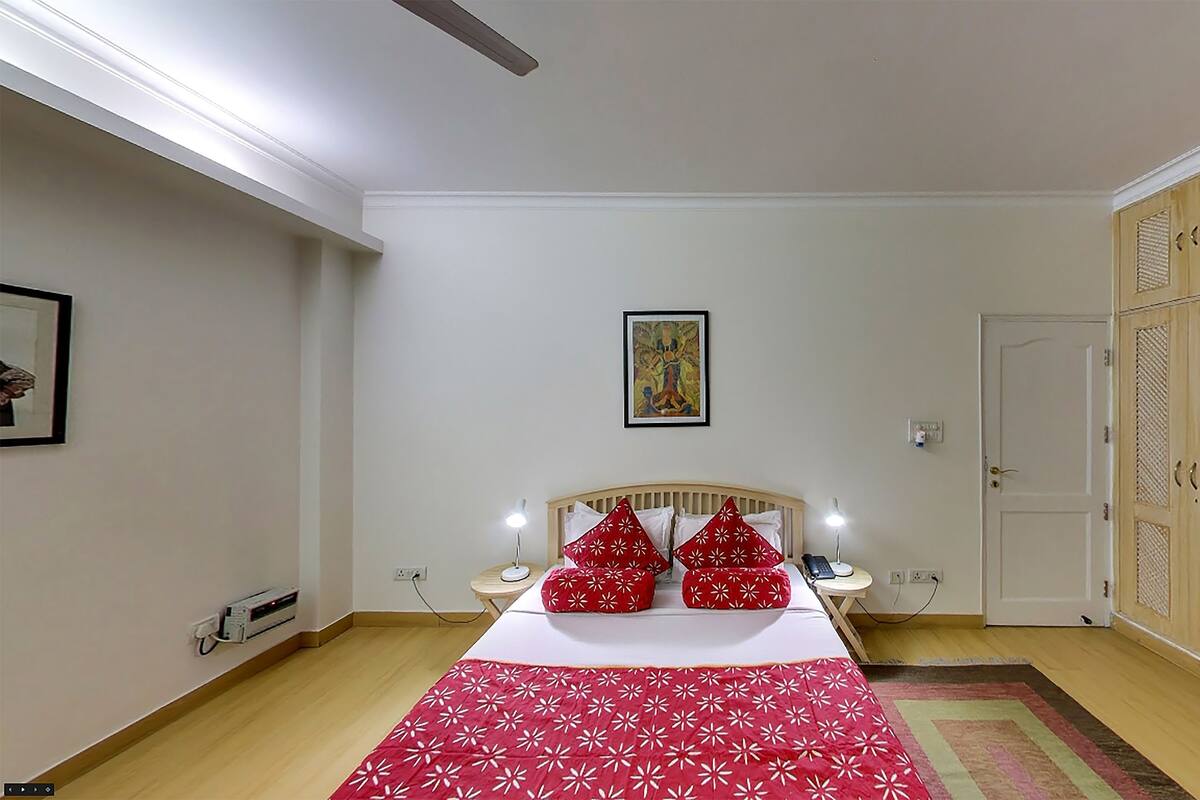 A bedroom with a bed, bedside lamps, a bedside table, a power outlet, a door, and a wardrobe.
