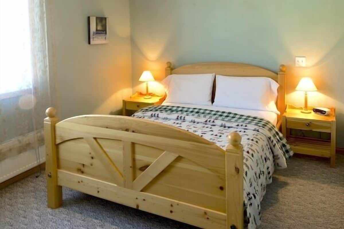 Ein hölzernes Bett mit karierter Bettdecke, zwei Nachttische mit Lampen und ein gerahmtes Bild an der Wand.