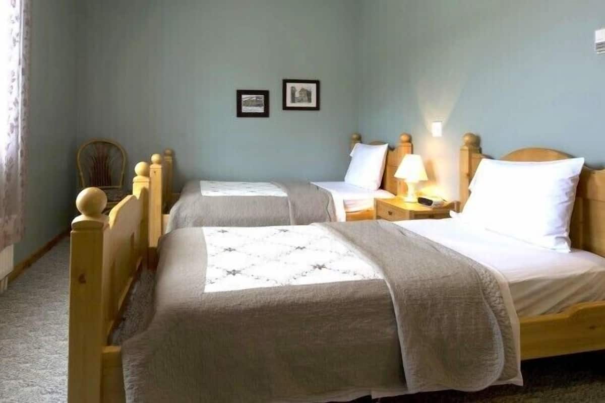 Ein Zimmer mit zwei Holzbett, einem Nachttisch mit Lampe und einem Fenster mit floralem Vorhang.