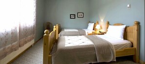 A room with two wooden beds, a nightstand with a lamp, and a window with floral curtains.