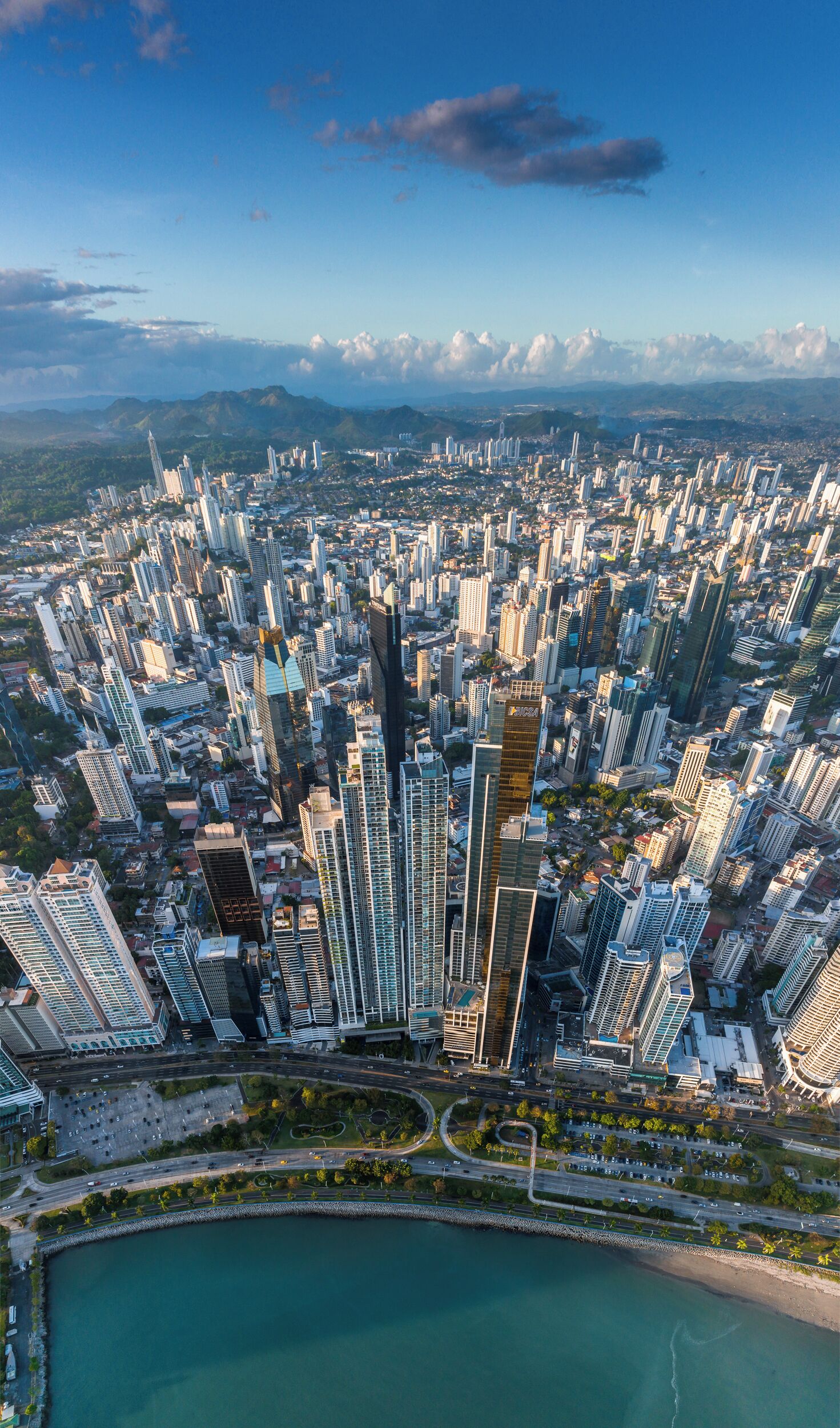 A dense urban skyline with high-rise buildings, a waterfront, and a clear sky.