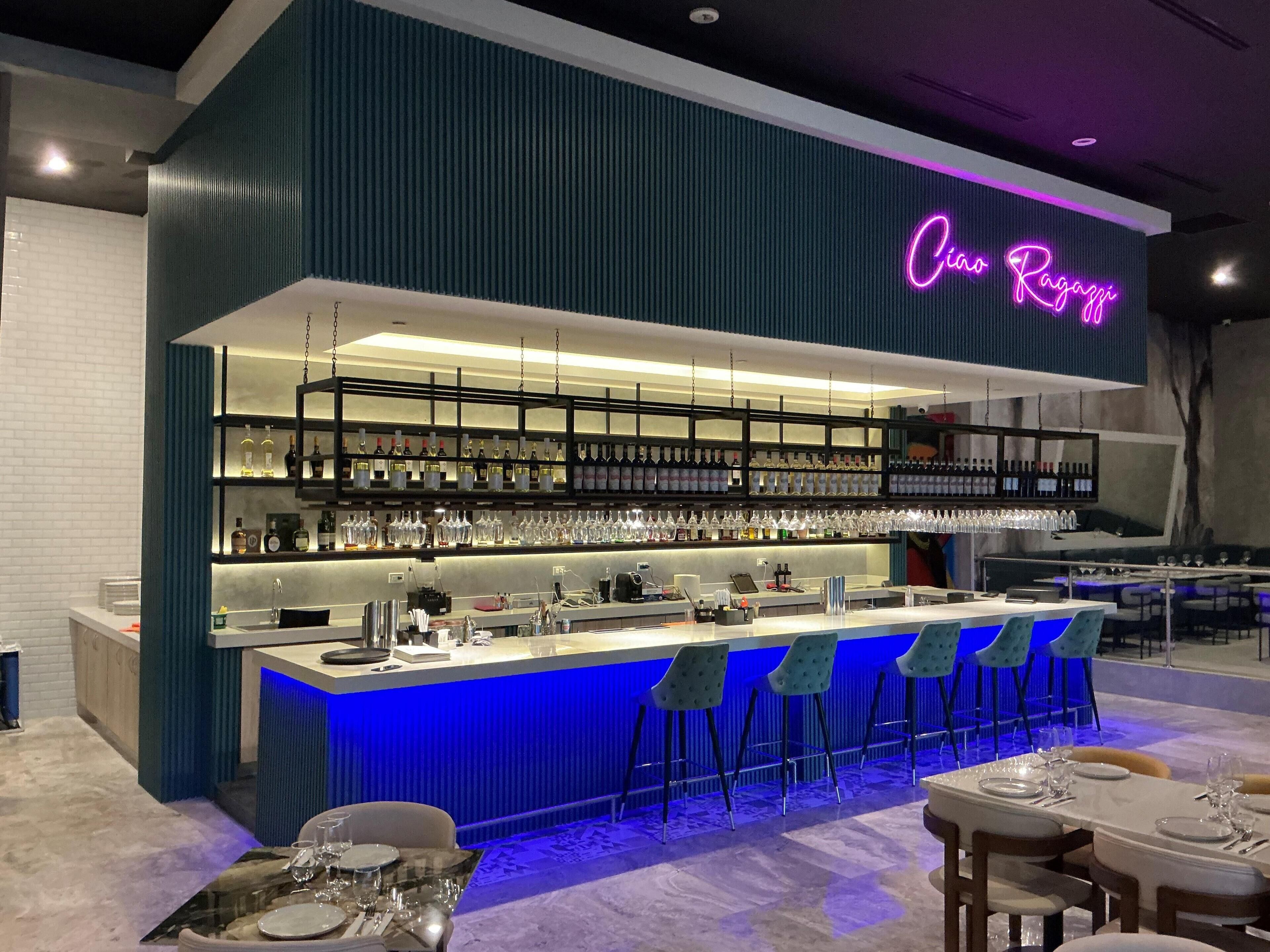 A modern bar area with a neon sign, shelves of bottles, and bar stools.