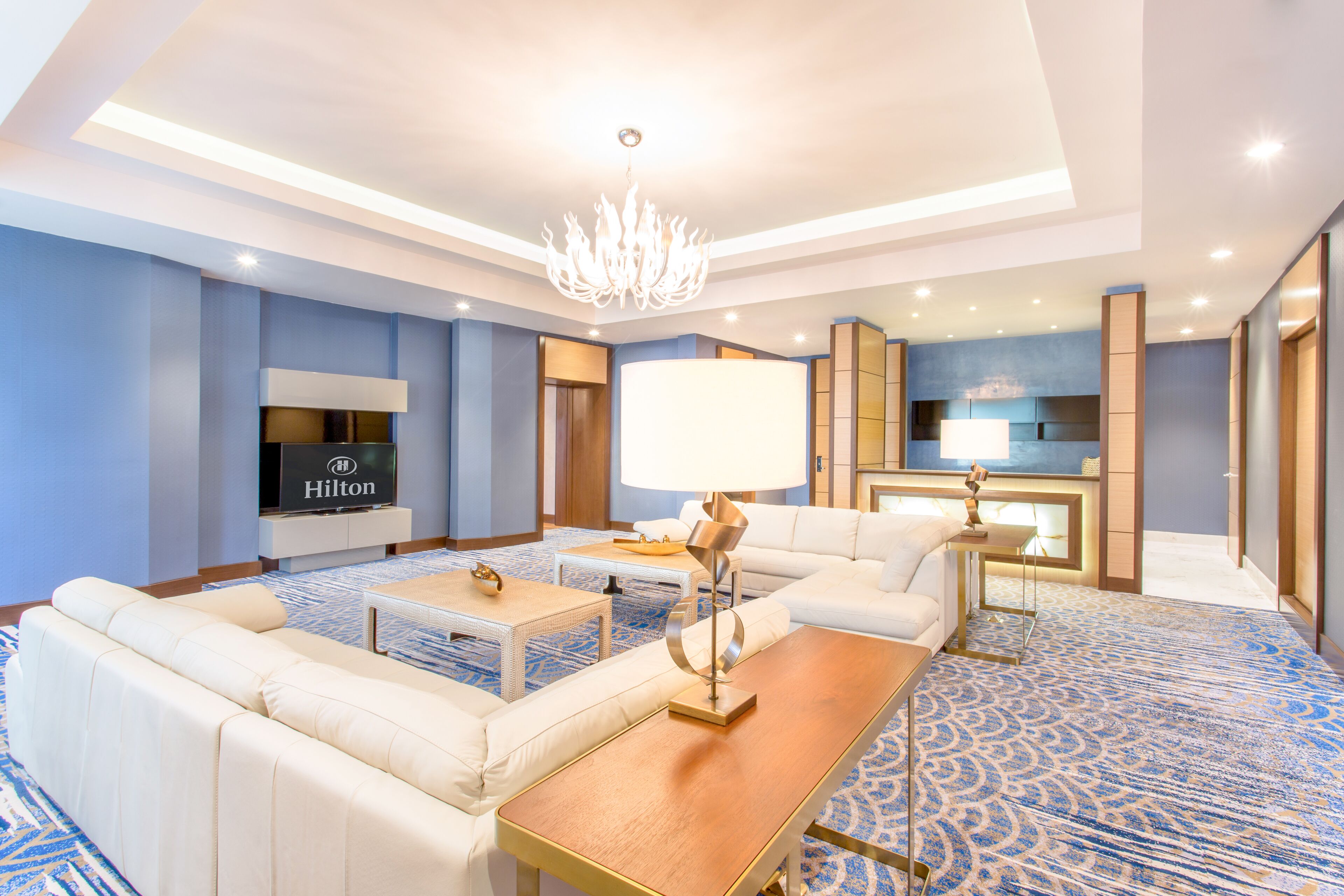 A modern hotel room with a sofa, coffee table, and a flat-screen TV.