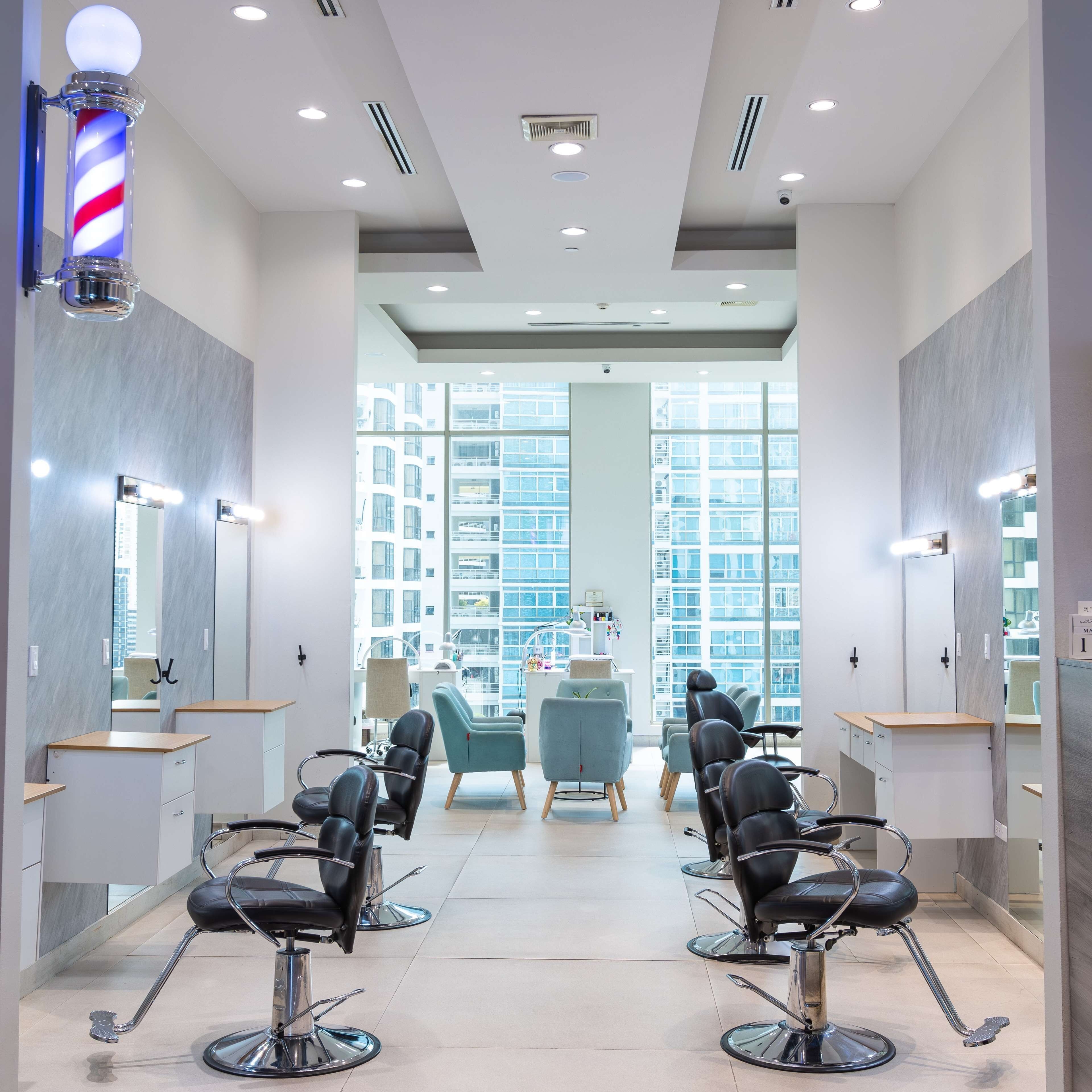 A modern hair salon with multiple barber chairs, large mirrors, and a view of tall buildings through large windows.