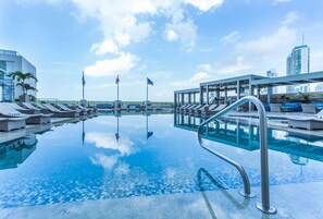 Zona de piscina con sillones de descanso y un área de estar cubierta, rodeada de edificios modernos.